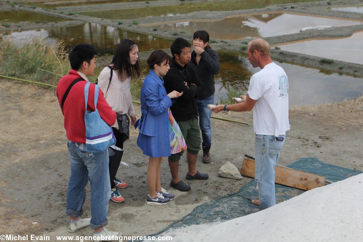 Le paludier Frédéric Lelant présente à l'équipe de tournage le sel gris et la fleur de sel. Maya Kobayashi porte un manteau bleu.