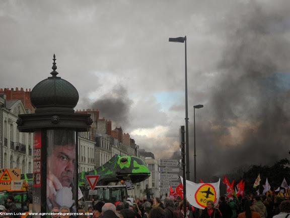 15h57. "Tracteur vigilant" équipé d'un spectaculaire triton géant, aux abords du square Daviais, terminus de la manifestation. Les fumées d'incendie sur la chaussée, à l'arrière-plan, marquent le contraste avec l'aspect festif de la manif. Manifestation anti-aéroport à Nantes le 22 février 2014. 15h57. "Tracteur vigilant" équipé d'un spectaculaire triton géant, aux abords du square Daviais, terminus de la manifestation. Les fumées d'incendie sur la chaussée, à l'arrière-plan, marquent le contraste avec l'aspect festif de la manif. Manifestation anti-aéroport à Nantes le 22 février 2014.