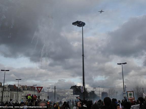 16h27. Nuages et fumées se confondent. Haut dans le ciel un avion en approche par l'est (côté terre). Cette approche est utilisée en fonction du vent dominant, en alternative à l'approche par l'ouest (côté mer). Manifestation anti-aéroport à Nantes le 22 février 2014. 16h27. Nuages et fumées se confondent. Haut dans le ciel un avion en approche par l'est (côté terre). Cette approche est utilisée en fonction du vent dominant, en alternative à l'approche par l'ouest (côté mer). Manifestation anti-aéroport à Nantes le 22 février 2014.
