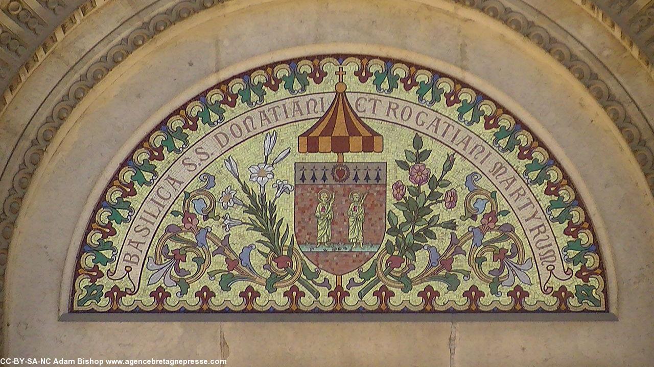 Fronton en mosaïque du portail central de la basilique. Donatien et Rogatien y sont représentés. Remarquer les hermines dans le blason. À droite le blason de Nantes, à gauche semis d'hermines. Fronton en mosaïque du portail central de la basilique. Donatien et Rogatien y sont représentés. Remarquer les hermines dans le blason. À droite le blason de Nantes, à gauche semis d'hermines.